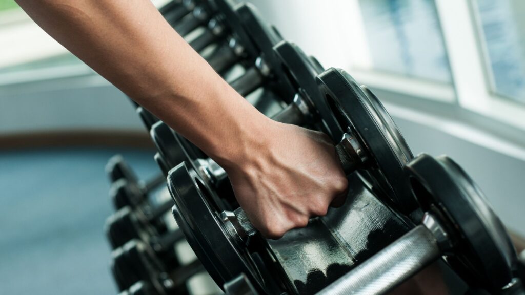 a person grabbing dumbbells from a rack indoors