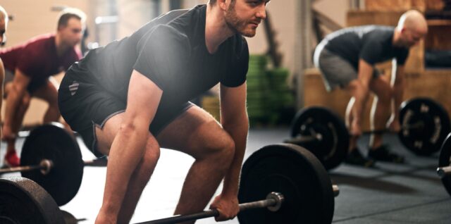 a man deadlifting a barbell with weight plates on it in a gym